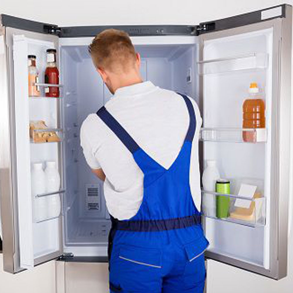 a man in overalls opening the door of a refrigerator.