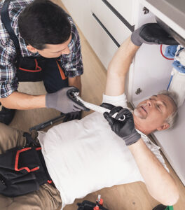 two men working on a sink in a kitchen.