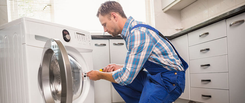 a man fixing a washing machine in a kitchen.