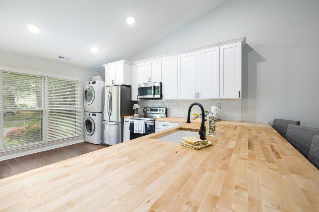 A white kitchen with wood counter tops and a washer and dryer.