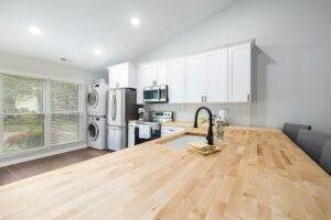 A white kitchen with wood counter tops and a washer and dryer.