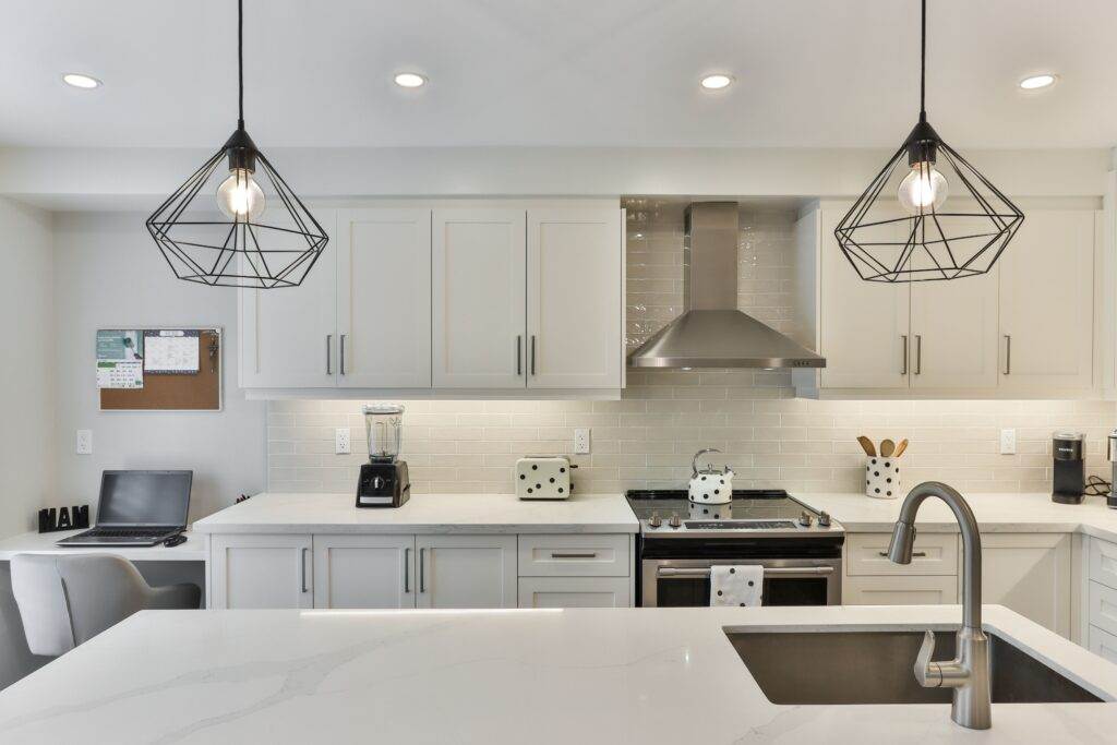 A white kitchen with stainless steel appliances and pendant lights.